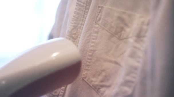 Close up de passar camisa branca com uma escova de vapor elétrica. Conceito. Home rotina, mulher mão vapor roupas no fundo embaçado. — Vídeo de Stock