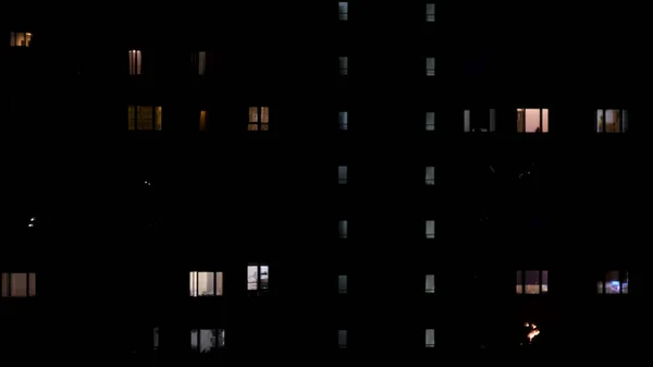 Vista noturna de luzes na janela do edifício de vários andares. Conceito. Casa de vários andares com apartamentos no final da noite, conceito de vida noturna. — Fotografia de Stock