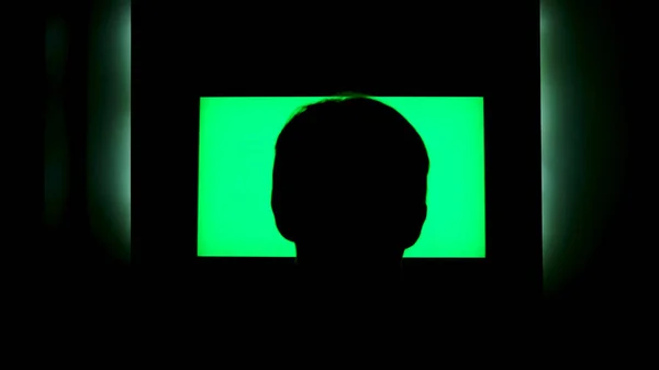 Bakifrån av en manlig huvud siluett framför tv med grön skärm. Begreppet. Man tittar på TV med kromakey som hänger på vågorna på natten hemma. — Stockfoto