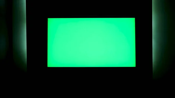 TV with horizontal green screen on a black wall with green illumination. Concept. Close up of chroma key TV screen in a dark room at night.
