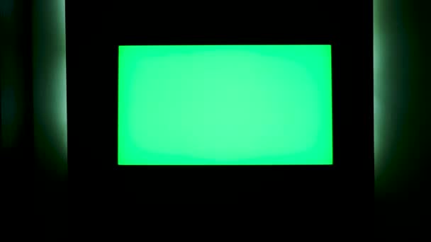 TV con pantalla verde horizontal en una pared negra con iluminación verde. Concepto. Primer plano de la pantalla de TV de croma key en una habitación oscura por la noche. — Vídeo de stock