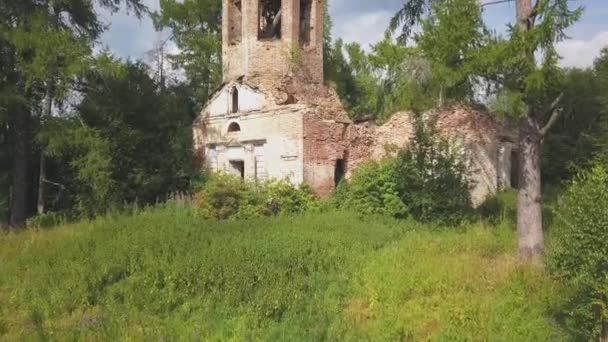 Iglesia abandonada en el bosque. Clip. Vista aérea de la antigua iglesia con un campanario y una cúpula en ruinas en el fondo de árboles verdes en colores brillantes y soleados. — Vídeo de stock