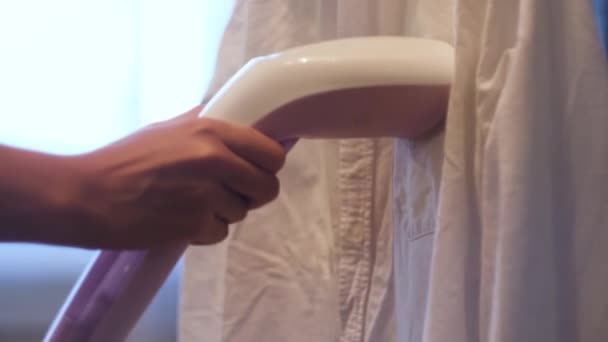 Woman hand ironing shirt with steam iron. Concept. Close up of a girl hands using steamer for ironing white shirt at home against the window. — Stock Video