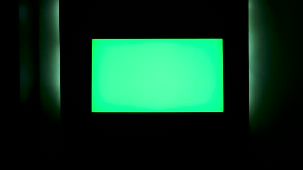 TV con pantalla verde horizontal en una pared negra con iluminación verde. Concepto. Primer plano de la pantalla de TV de croma key en una habitación oscura por la noche. — Vídeo de stock