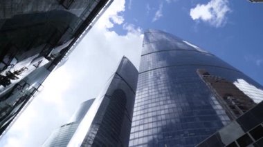 Arka plandaki cam gökdelenlerin alt görüntüsü mavi gökyüzü. Başla. Modern şehrin merkezindeki yüksek katlı işletmelerin baş döndürücü manzarası. Cam gökdelenler mavi gökyüzünü yansıtır