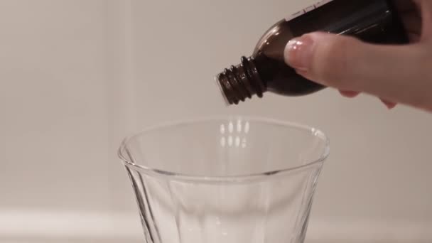 Detailní záběr léku kapajícího z láhve do čirého skla. Koncept. Žena kapky lék do skla na bílém izolovaném pozadí. Léčba nebo jed — Stock video