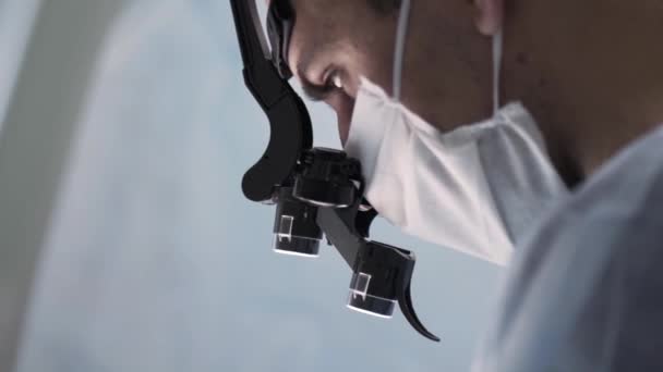 Surgeon head with professional glasses at work. Action. Close up side view of a doctor in glasses with binocular magnifiers examines something at laboratory. — Stock Video