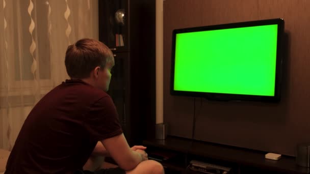 O homem olha para o ecrã verde da TV. Conceito. O homem está sozinho a ver televisão de ecrã verde em casa. Homem olha para TV tela verde com interesse — Vídeo de Stock