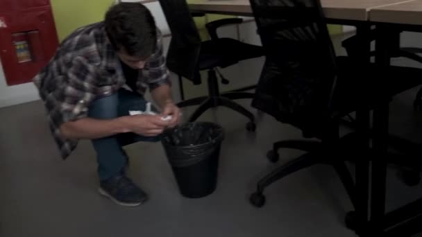 Un hombre mirando algo en un cubo de basura. Imágenes de archivo. Hombre tomando hojas blancas arrugadas de papel de un cubo de basura y leyendo información, concepto del trabajo de oficina. — Vídeo de stock