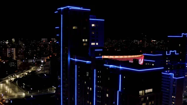 Widok z lotu ptaka na duży widok na miasto, koncepcja życia nocnego. Materiał filmowy. Niesamowity wysoki budynek z niebieskim neonowym oświetleniem fasady na nocnym krajobrazie miasta z wieloma światłami. — Zdjęcie stockowe