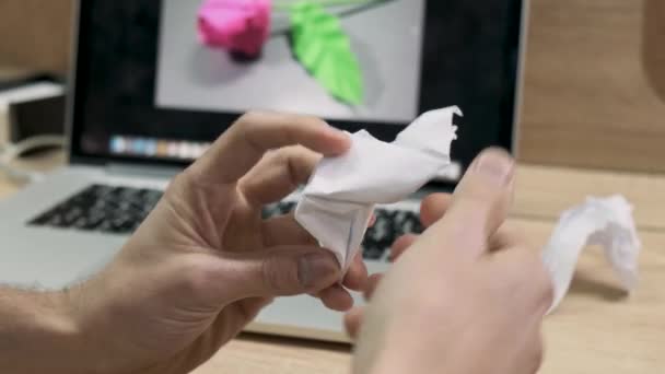 Mãos masculinas fazendo origami figura de papel branco. Imagens de stock. Homem não consegue fazer uma flor de papel como em uma imagem em uma tela do computador, — Vídeo de Stock