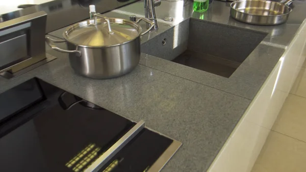 Close-up van inductie kookplaat, zwart glas op grijs aanrecht. Huishoudelijke gebruiksvoorwerpen. Details van nieuwe keuken, zilverkleurige pan en gootsteen. — Stockfoto