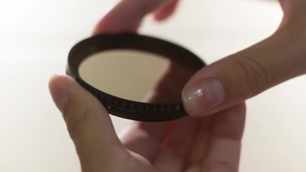 Close-up van polariserende lens filter in meisjes handen geïsoleerd op witte achtergrond. Concept. Vrouw die in het beide zijmechanisme van lensfilter verandert. — Stockvideo