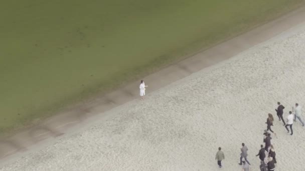 Widok z lotu ptaka przesłuchania młodej kobiety stojącej samotnie nad morzem przez prasę medialną. Materiał filmowy. Reporterzy biegnący w kierunku kobiety w białej sukni, koncepcja znanych mediów. — Wideo stockowe