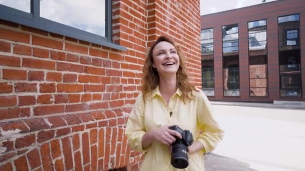 Femme photographe rit à la séance photo de rue. L'action. Belle femme tient caméra professionnelle et rit sur le mur de briques de fond — Video