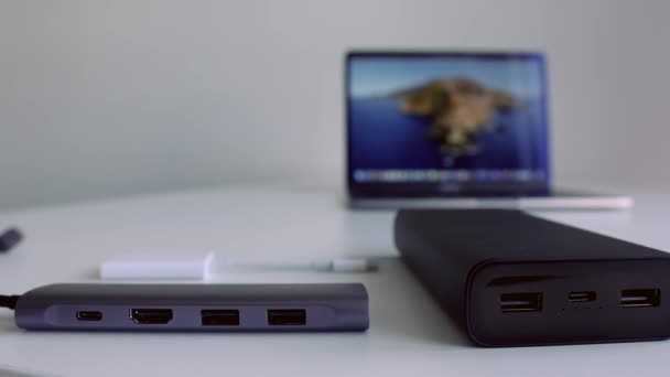 Hordozható töltő mobil eszközök hátterében fehér asztal és egy laptop. Felvétel. Elektromos banki eszközök és egy asztalon fekvő számítógép közelsége. — Stock videók
