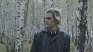 Genç adam ormana bakıyor. Hisse. Genç adam ormana sert bir bakışla bakıyor. Manyakça görünüşlü bir adam ormanda birini arıyor.