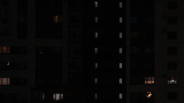 Janelas de edifício residencial com pessoas à noite. Conceito. Vida noturna em janelas de edifício de vários andares. Janelas luminosas e escuras no edifício residencial — Fotografia de Stock