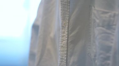 Beyaz gömleği elektrikli buhar fırçasıyla ütüle. Kavram. Ev rutini, kadın eli buharlı giysiler bulanık arka planda..