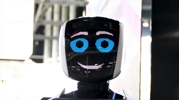 Funny robot with big blue eyes smiling and talking. Meida. Close up of robot face screen with friendly smile at the exhibition of modern technologies.