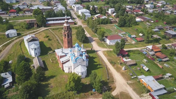 Luftaufnahme eines Dorfes in ökologischem Gebiet mit vielen Häusern und einer Kirche. Clip. Ländliche leere Straße, die zum Dorf auf blauem wolkenverhangenem Himmel führt. — Stockfoto