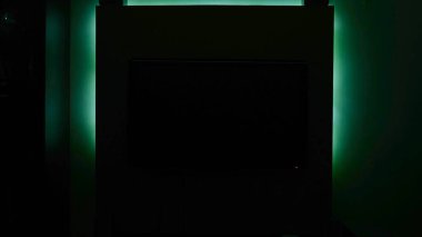 Duvarın arkasındaki ışık karanlıkta parlar. Kavram. Televizyon kapalı ve yeşil ışıklı duvara asılıyor. Neon iç aydınlatma gecenin karanlığında parlar.
