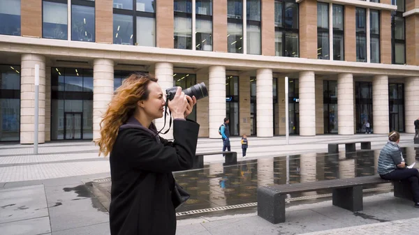 Woman takes photos with professional camera of business building. Action. Beautiful woman photographer shoots urban modern architecture