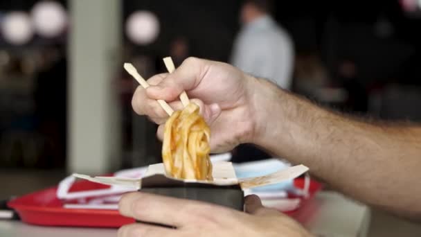 Close-up van mannelijke handen met houten Chinese eetstokjes die heerlijke Aziatische wok noedels eten. De media. Zijaanzicht van het eten van Chinese pasta op een openbare plaats. — Stockvideo