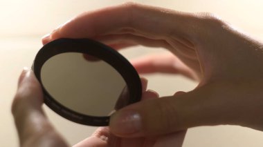 Kadın eli beyaz arka planda kamera merceği filtresi tutuyor. Kavram. Kadın ellerinin yuvarlak şekilli kamera filtresi açıp kapamasını kapat.