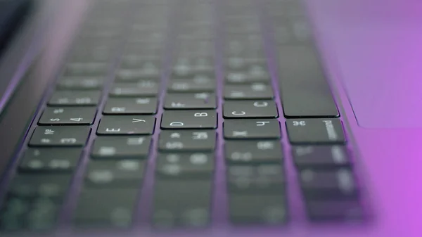 Side view of laptop or computer details, black keyboard with white symbols. Action. Extreme close up of backlit keyboard with flowing camera focus.