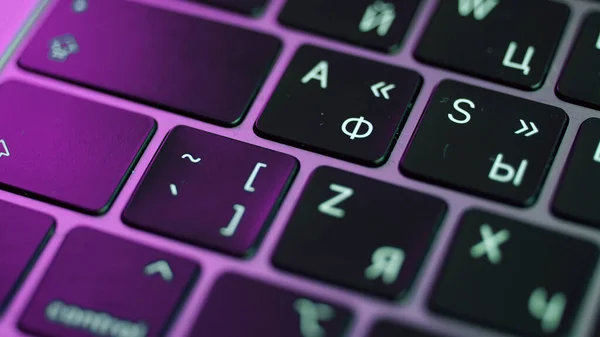 Primer plano del ordenador portátil o teclado de la computadora. Acción. Concepto de dispositivos y tecnologías modernas, botones de un teclado negro bajo la luz púrpura. —  Fotos de Stock