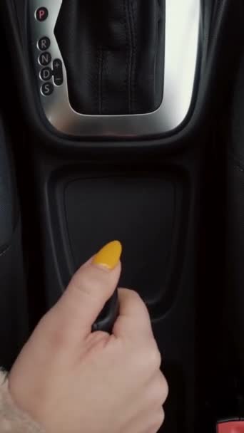 Fechar-se de preparações antes de deixar um carro. Acção. Visão vertical superior de uma mulher com manicure amarelo levantando o freio de mão e definindo a alavanca de mudança de engrenagem automática. — Vídeo de Stock