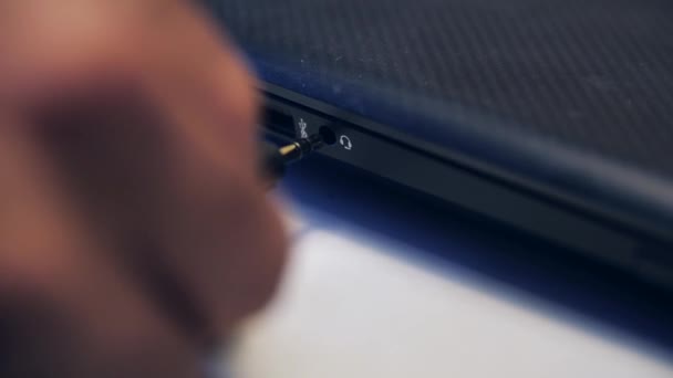 남자 손을 감고 컴퓨터나 노트북 포트에 헤드폰 케이블을 꽂는다. 미디어. 흰 배경에 분리 된 장치에 케이블을 연결하는 모습. — 비디오