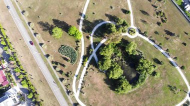 Sarı otlarla dolu bir araziyi geçen dar yolları kıvırmak. Şarjör. Etrafı çalılarla ve kuru çayırlarla çevrili yeşil göletli küçük bir şehir manzarası..