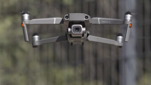 Dron s kamerou vznášející se ve vzduchu. Akce. Detailní záběr letadla a ostří, které se otáčí ve zpomaleném pohybu na rozmazaném pozadí zelených stromů, fotografování. — Stock video