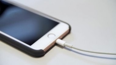 Beyaz masada duran şarj kablosu olan elmalı iPhone 'u kapat. Medya. usb kablosuna bağlı modern bir aygıtın şarj işlemi.