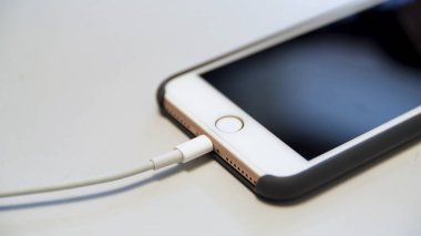 Beyaz masada duran şarj kablosu olan elmalı iPhone 'u kapat. Medya. usb kablosuna bağlı modern bir aygıtın şarj işlemi.