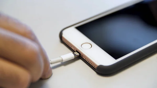 Gros plan de l'iphone pomme avec le câble de charge couché sur la table blanche. Les médias. Processus de charge d'un appareil moderne connecté au câble USB. — Photo