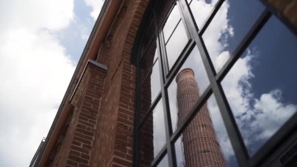 Antigua chimenea de Moscú Arma barrio de negocios se refleja en una ventana. Acción. Vista inferior de una pared de ladrillo rojo de una antigua fábrica de gas con una chimenea alta sobre fondo azul nublado del cielo. — Vídeos de Stock