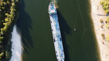 Yeşil kanallı bir kargo gemisinin yukarıdan görünen görüntüsü. Görüntü. Nehirde yüzen uzun, beyaz bir gemi. İnsanlar sahilde eğleniyor ve banyo yapıyor..