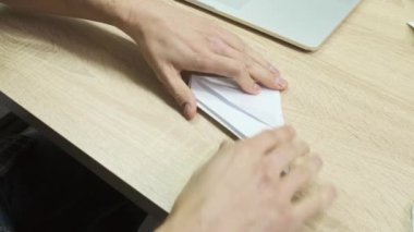 Uçak yapmak için kağıt katlayan bir adamın eli. Stok görüntüleri. Yaratıcı faaliyetler kavramı, erkek eli kapalı tahta bir masada origami yapıyor..