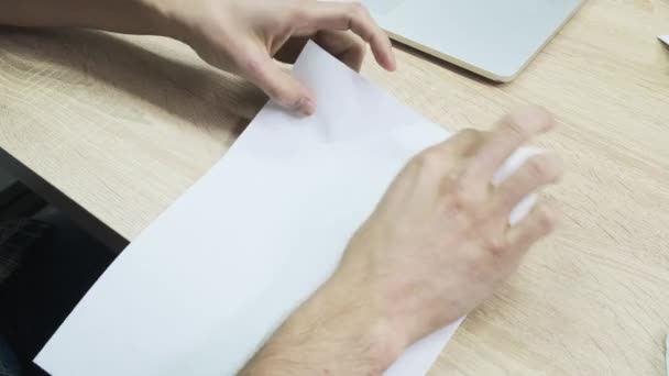 Κάτοψη των αρσενικών χεριών που προσπαθούν να φτιάξουν ένα αεροπλάνο από ένα φύλλο χαρτί. Στικ. Κοντινό πλάνο του ανθρώπου χέρια εξάσκηση origami σε ξύλινο τραπέζι φόντο. — Αρχείο Βίντεο