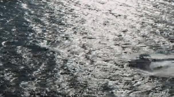 Słońce odbija się w powierzchni wody i motorówka szybko pływa. Postrzelony. Widok z powietrza małej łodzi motorowej przechodzącej przez fale Morza Czarnego w letni słoneczny dzień. — Wideo stockowe