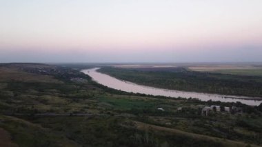 Küçük bir köyü, ormanı ve nehri olan yaz kırsal arazisi, hava manzarası. Görüntü. Bereketli yeşil çayırlar ve tarım arazileri olan doğal manzara, gün batımında bir nehir ve bir köy..