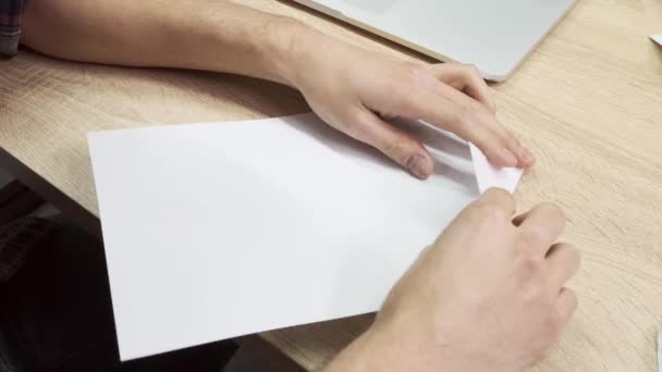 折り紙の図を作る手。ストック映像だ。木製のテーブルの背景に折り紙を作るための紙の白いシートを使用して男性の手の閉じる,創造性の概念. — ストック動画
