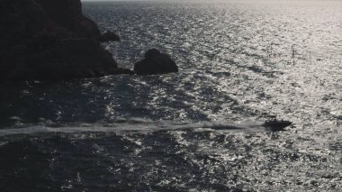 Denizde motorlu teknesi olan Rocky takımadaları, doğal manzara. Vuruldu. Uçurumun kenarından geçen bir sürat teknesinin havadan görünüşü güneşli bir günde dalgaların üzerinde zıplamak, lüks ve spor kavramı..