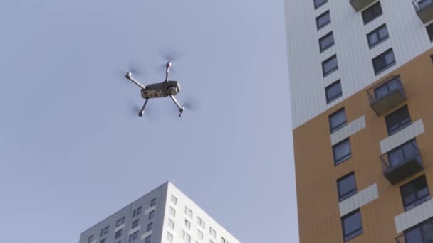 Drone flying in the city street in the summertime. Action. Bottom view of a flying quadcopter near high rise buildings on blue sky background. — Stock Video