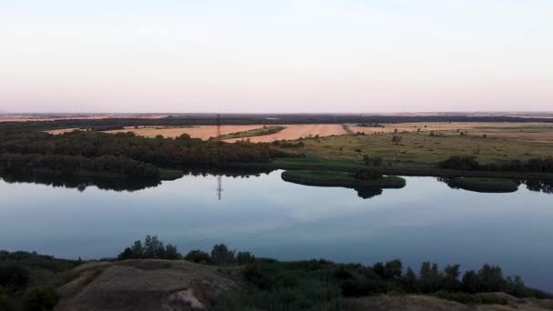 Widok z lotu ptaka na zakręty rzeki wzdłuż pól uprawnych. Nagranie. Wspaniały panoramiczny widok z lotu ptaka na naturalny krajobraz z bujnymi łąkami i rzeką o zachodzie słońca. — Wideo stockowe