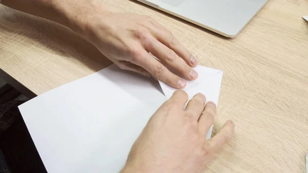 Χέρια που φτιάχνουν οριγκάμι. Στικ. Κοντινό πλάνο των αρσενικών χεριών χρησιμοποιώντας ένα λευκό φύλλο χαρτί για την κατασκευή origami σε ξύλινο φόντο τραπέζι, έννοια της δημιουργικότητας. — Φωτογραφία Αρχείου