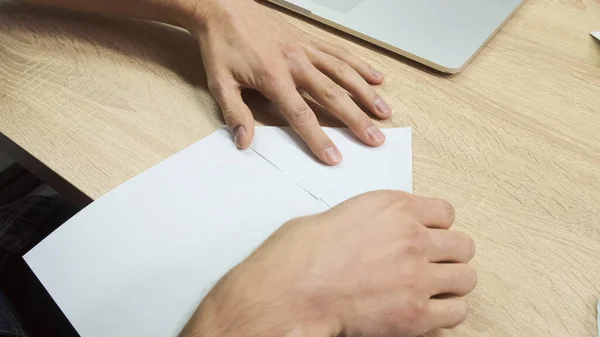 Κάτοψη των αρσενικών χεριών που προσπαθούν να φτιάξουν ένα αεροπλάνο από ένα φύλλο χαρτί. Στικ. Κοντινό πλάνο του ανθρώπου χέρια εξάσκηση origami σε ξύλινο τραπέζι φόντο. — Φωτογραφία Αρχείου